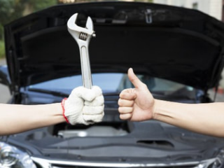 mobile mechanic holding wrench and giving thumbs up in front of a car with the hood open
