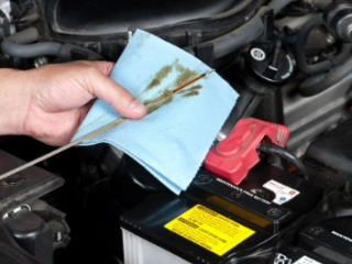 mobile mechanic checking oil in car and wiping oil off the dip stick