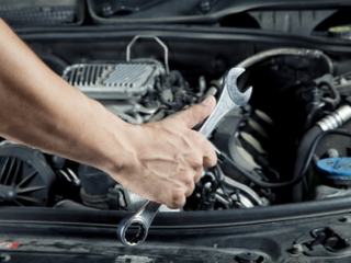 mobile mechanic holding a wrench as he works on the engine of a car